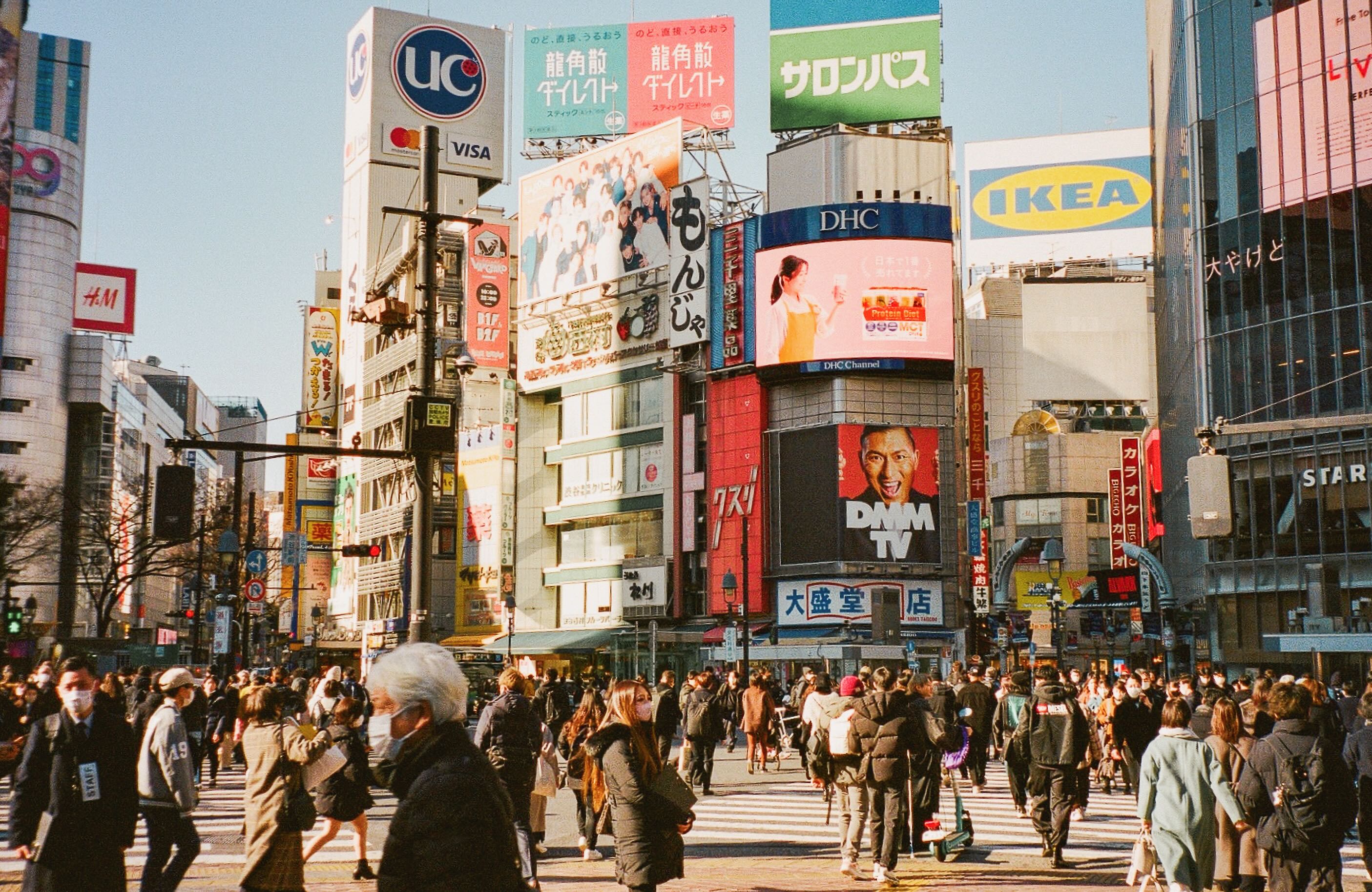 Crowds crossing shibuya crossing beneath colorful billboards in tokyo.