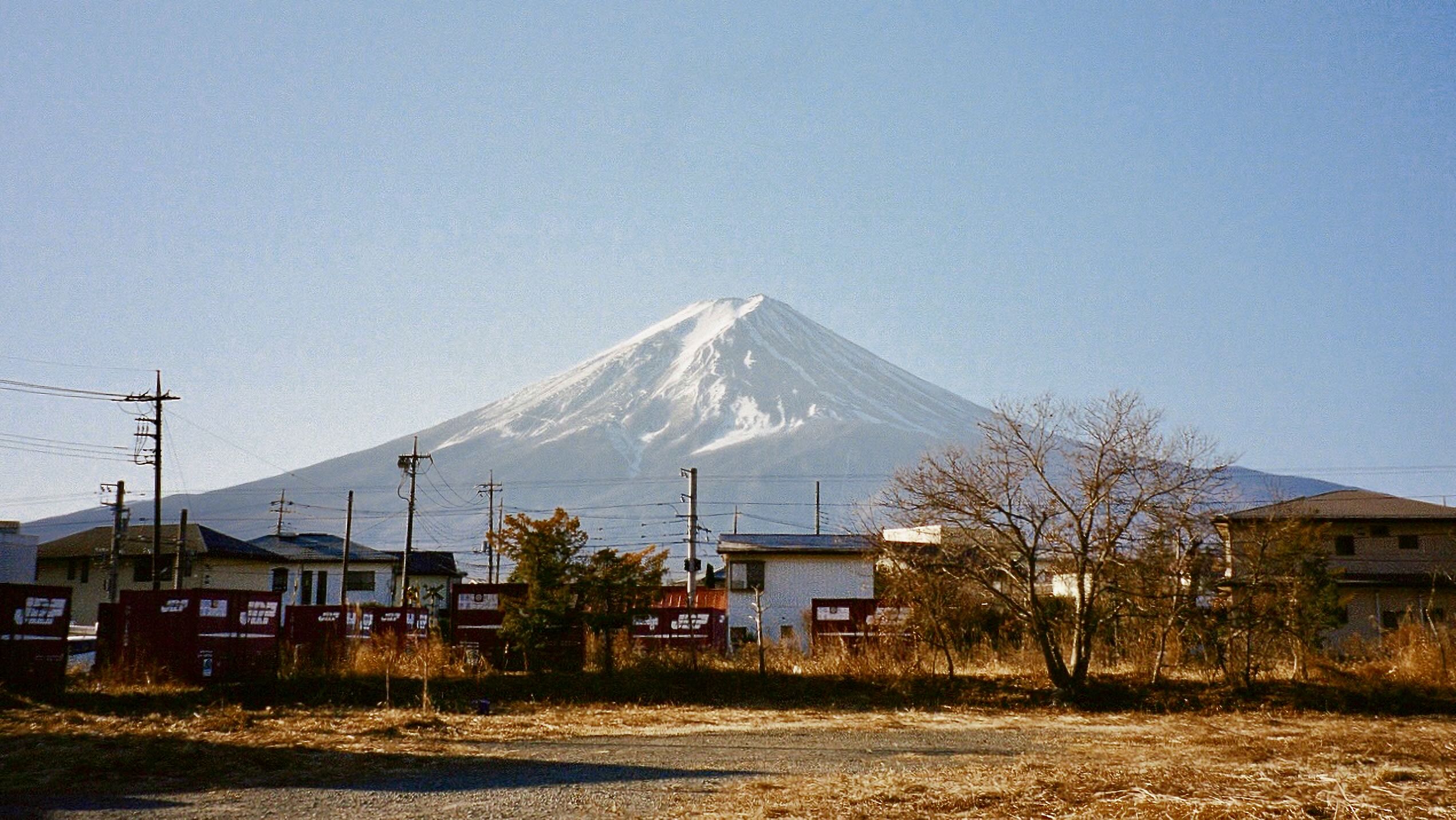 Snow-covered mount fuji rising above houses and utility lines in fujikawaguchiko.
