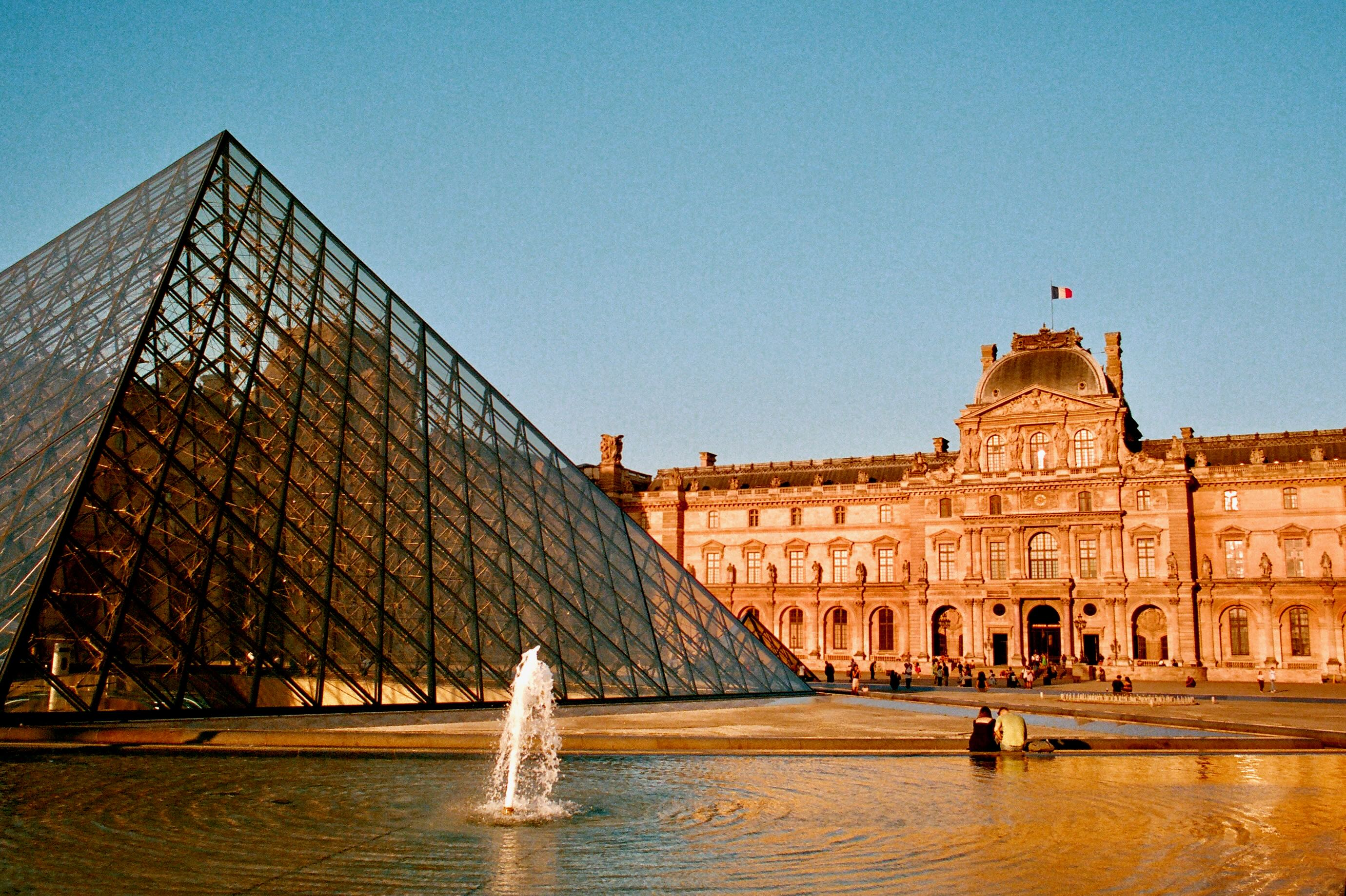 The glass louvre pyramid and courtyard fountain in warm sunlight.
